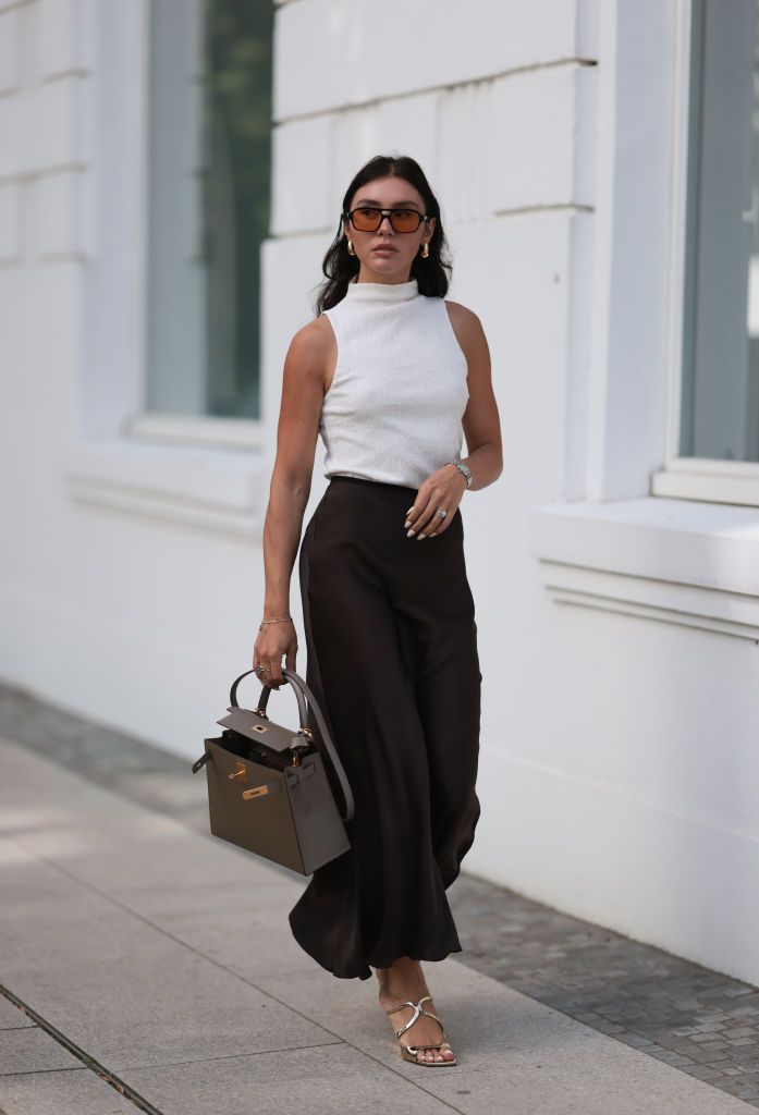 HAMBURG, GERMANY - AUGUST 22: Milena Karl is seen wearing black sunglasses with orange lenses from Lexxola, golden earrings from Bottega Veneta, a creme-white sleeveless top from Zara with turtle-neck, a black maxi skirt from Massimo Dutti, the Kelly bag from Hermes in grey-brown leather, golden and silver rings, a silver watch and shiny golden strap sandals with wedge heels from Jimmy Choo on August 22, 2023 in Hamburg, Germany. (Photo by Jeremy Moeller/Getty Images)