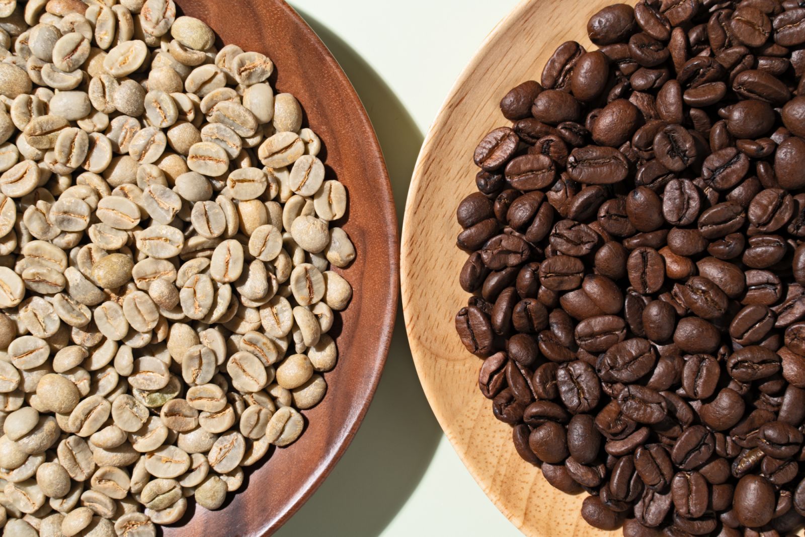 Raw Coffee Beans Vs. Roasted Coffee Beans on Green Background Close-up View.