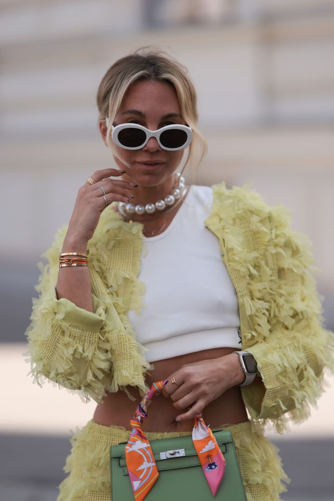 VIENNA, AUSTRIA - MAY 01: Karin Teigl wearing Celine white round shades, Miu Miu black leather thong ankle boots, Baum & Pferdgarten matching yellow cropped feather jacket and long midi skirt, CYK white cropped bra top, Hermes pastell green leather Kelly bag and Julia Skergeth big Pearl chain on May 01, 2023 in Vienna, Austria. (Photo by Jeremy Moeller/Getty Images)