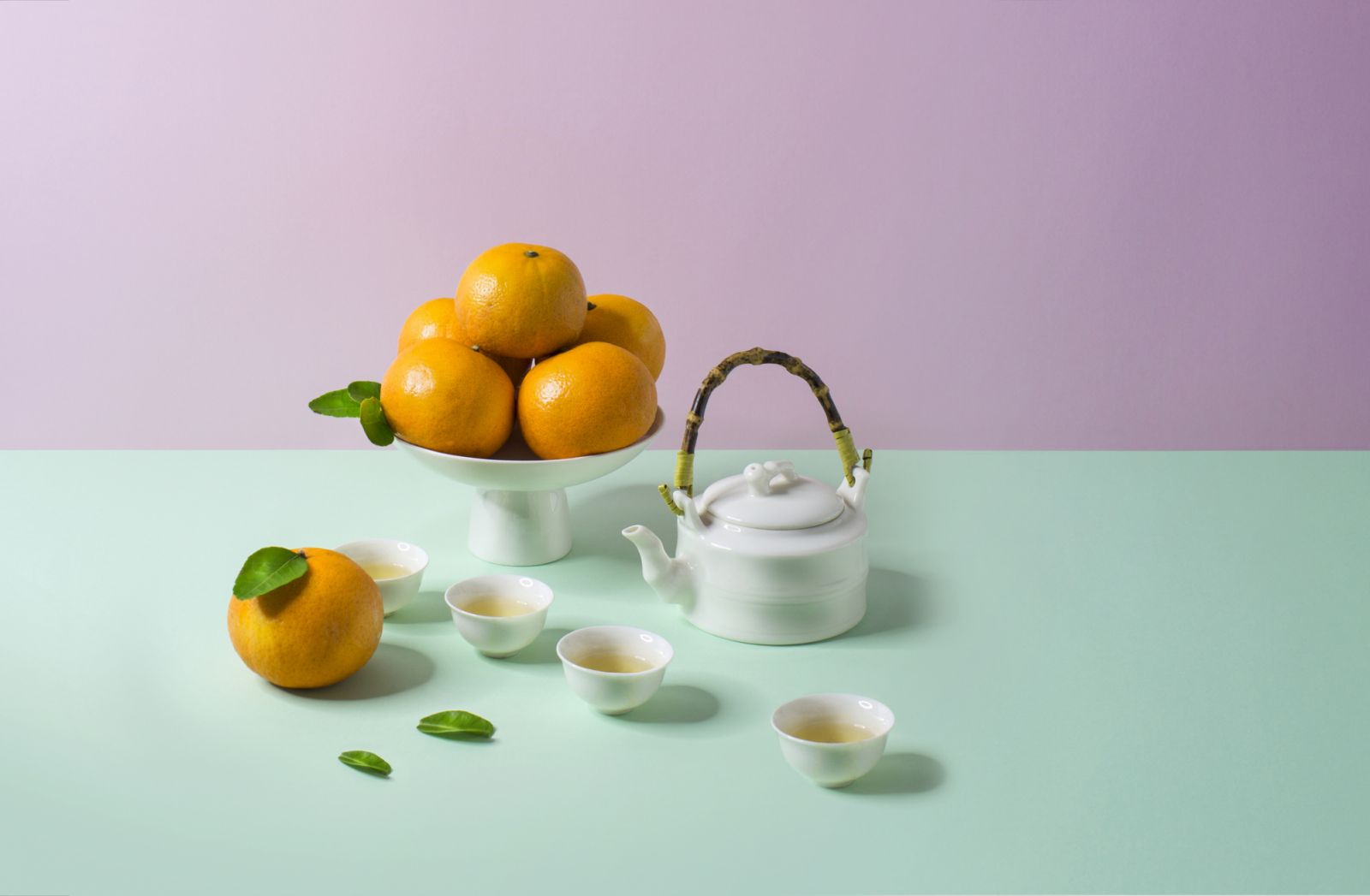 Pile of tangerine and tea set on pastel colored background.
