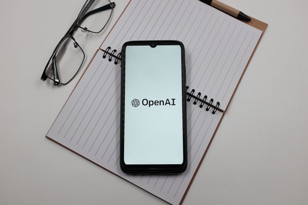 In this photo illustration an OpenAI logo is displayed on a smartphone screen above a notebook next to glasses in Athens, Greece on March 26, 2023. (Photo illustration by Nikolas Kokovlis/NurPhoto via Getty Images)