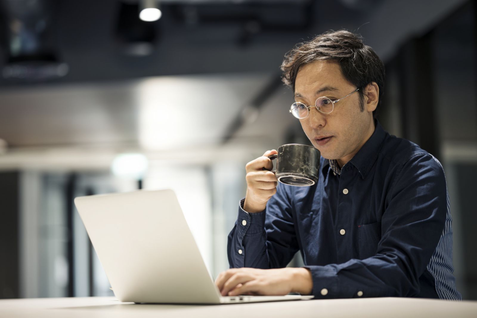 Side View of Japanese Businessman using a laptop while reading email and drinking coffee in a modern office. Business Mobility.