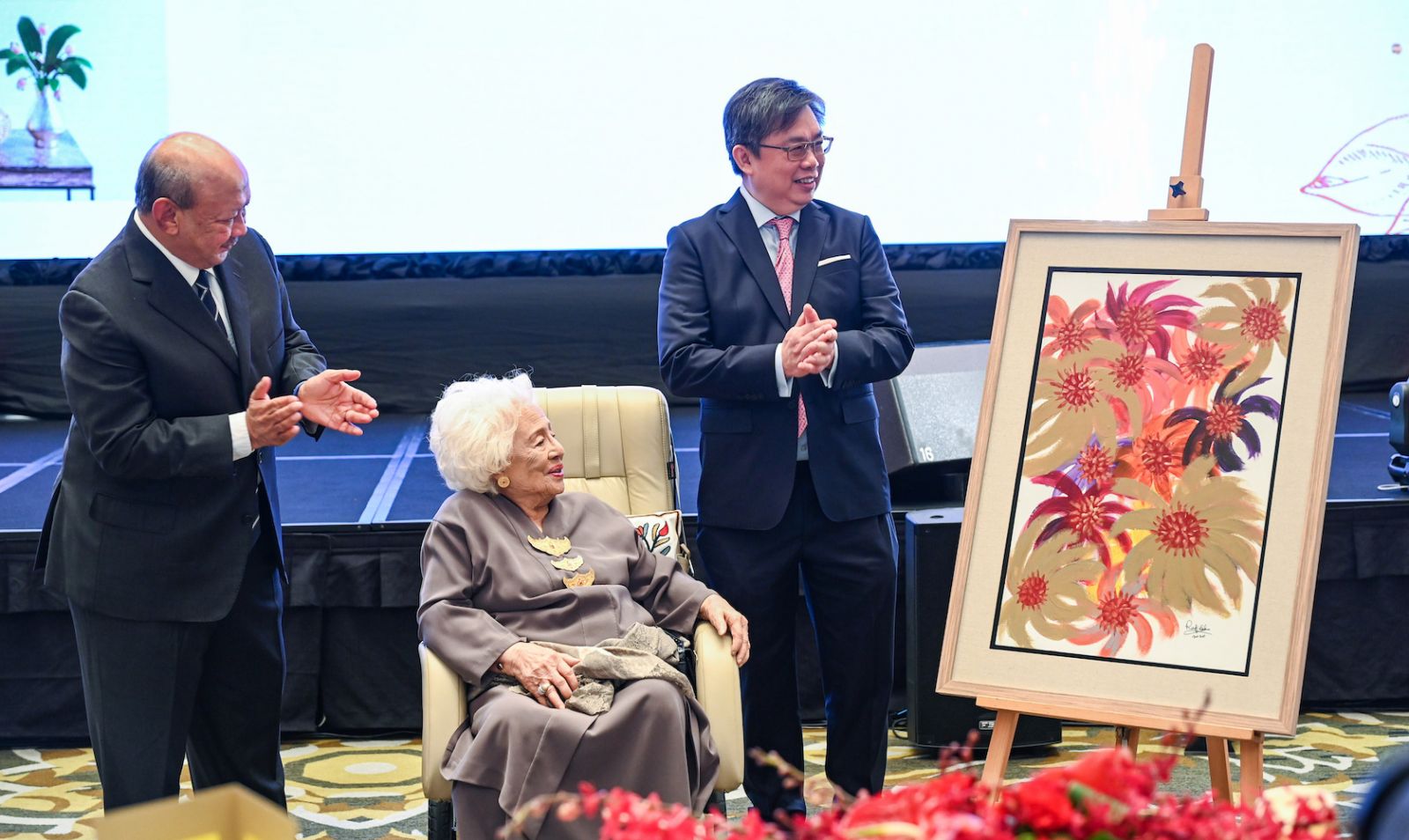 Kenanga Investment Bank chairman of the board Tan Sri Dato’ Seri Syed Anwar Jamalullail and Datuk Chay Wai Leong, Group Managing Director of Kenanga Investment Bank Berhad (right) presented Tengku Noor Zakiah with a painting by Tan Sri Rafidah Aziz (Photo Kenanga Group)