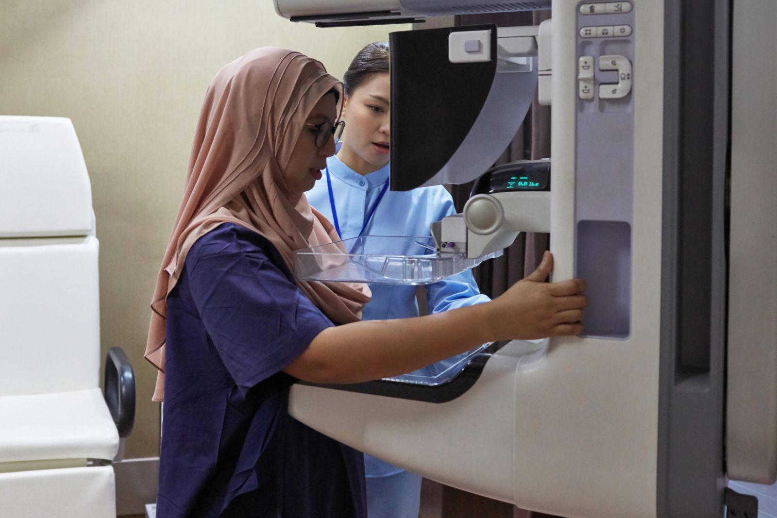 Nurse examining patient with medical equipment. Female healthcare worker is assisting woman during mammogram test. They are standing at hospital.