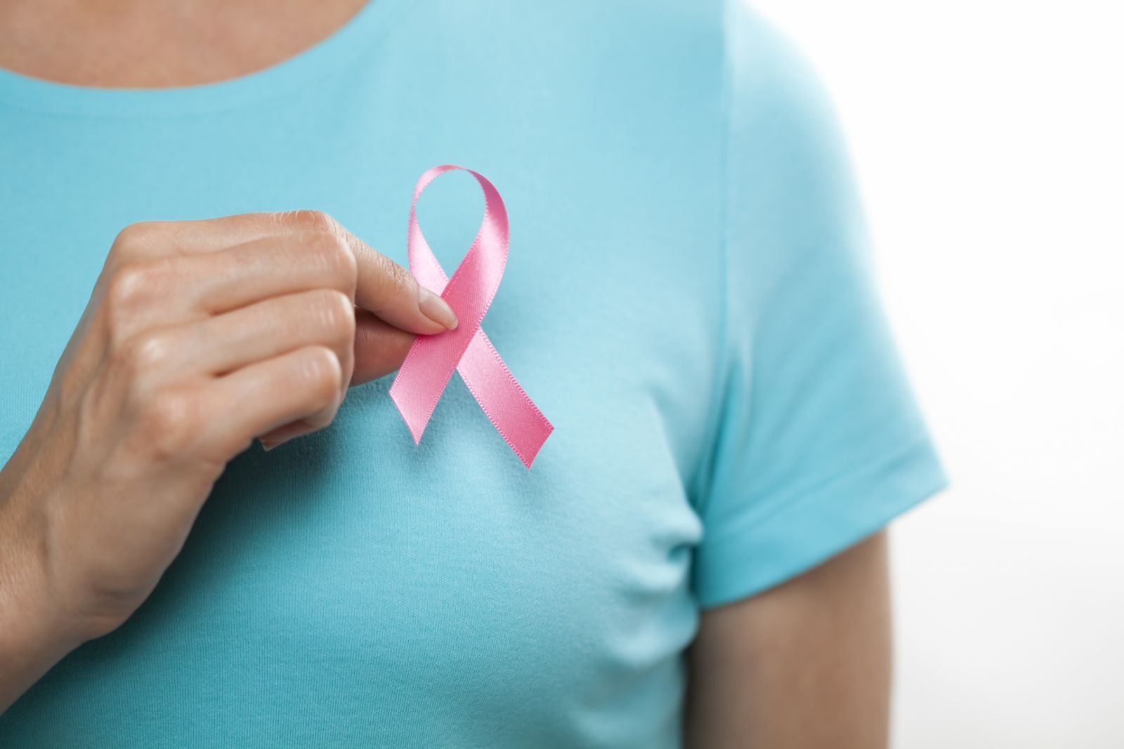 Woman putting on a pink breast cancer awareness ribbon. You may also like: