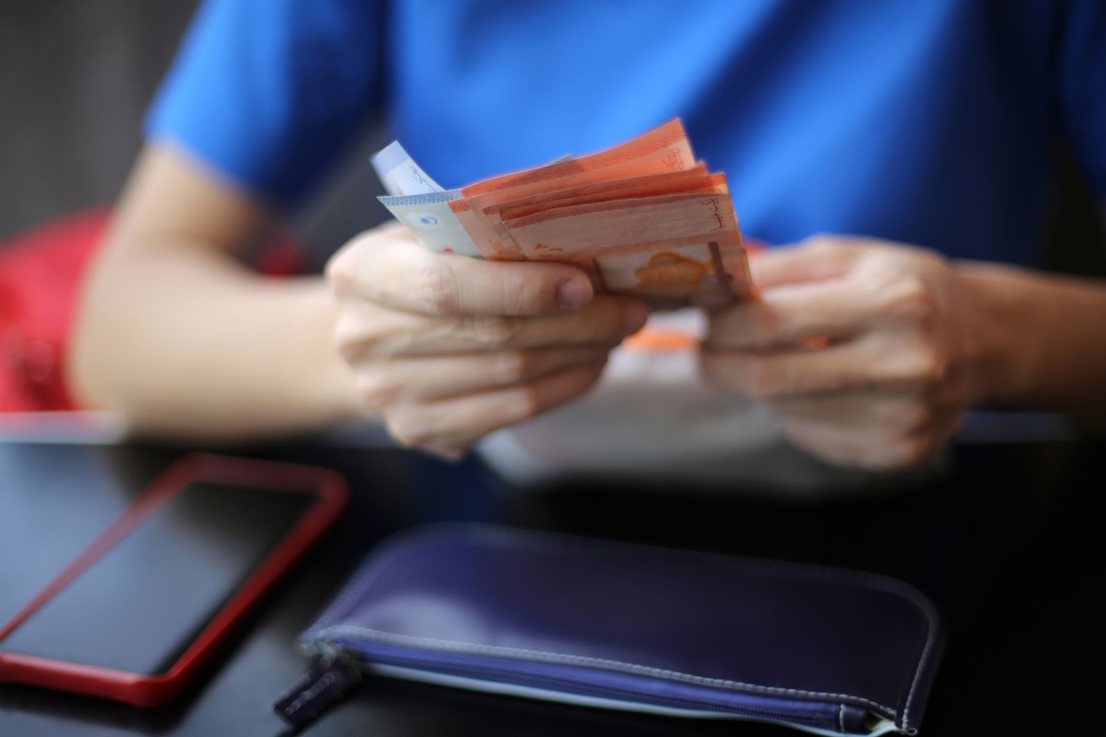 An Asian woman is counting Malaysian Ringgit (RM), RM10 and RM1 bank notes