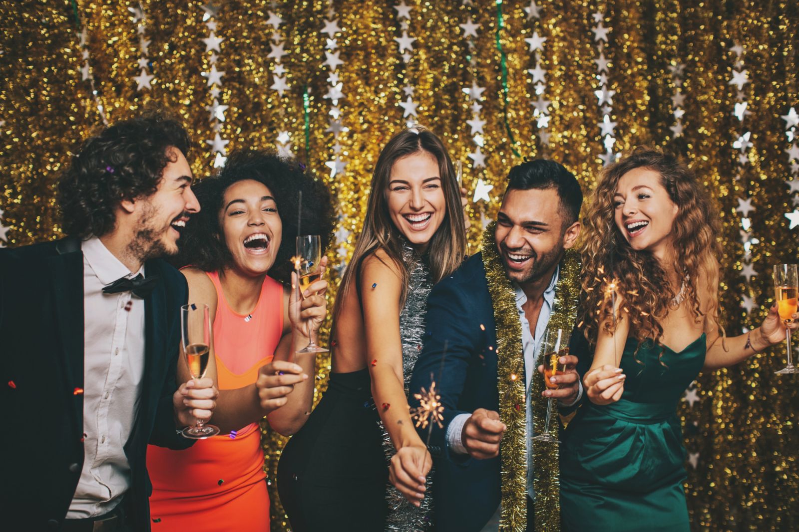 Multi-Ethnic group of cheerful people in formal wear holding chanpagne glasses and sparklers at New Year's celebration.