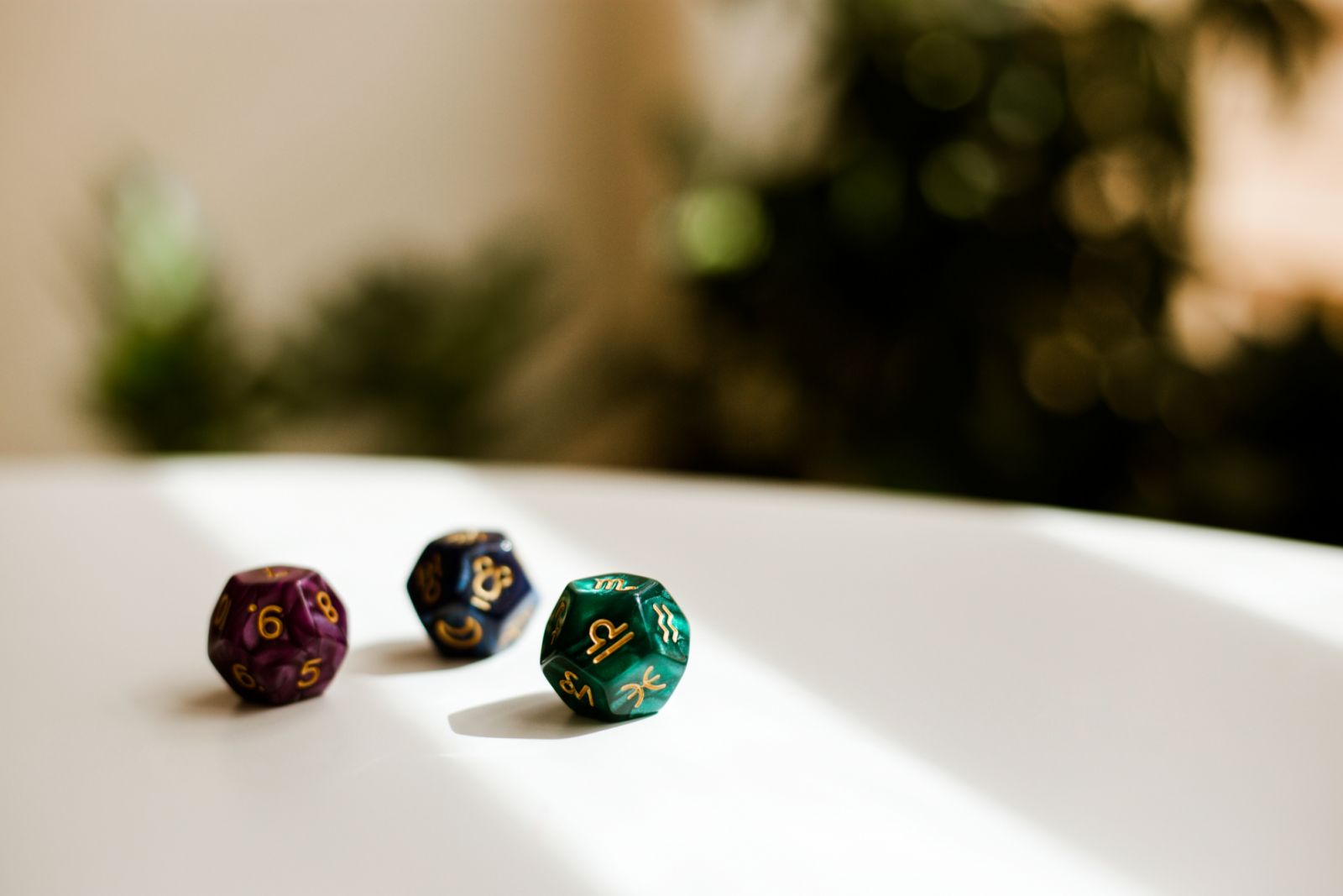 Coloured divination dice on white table with blurred plants and wall on background.