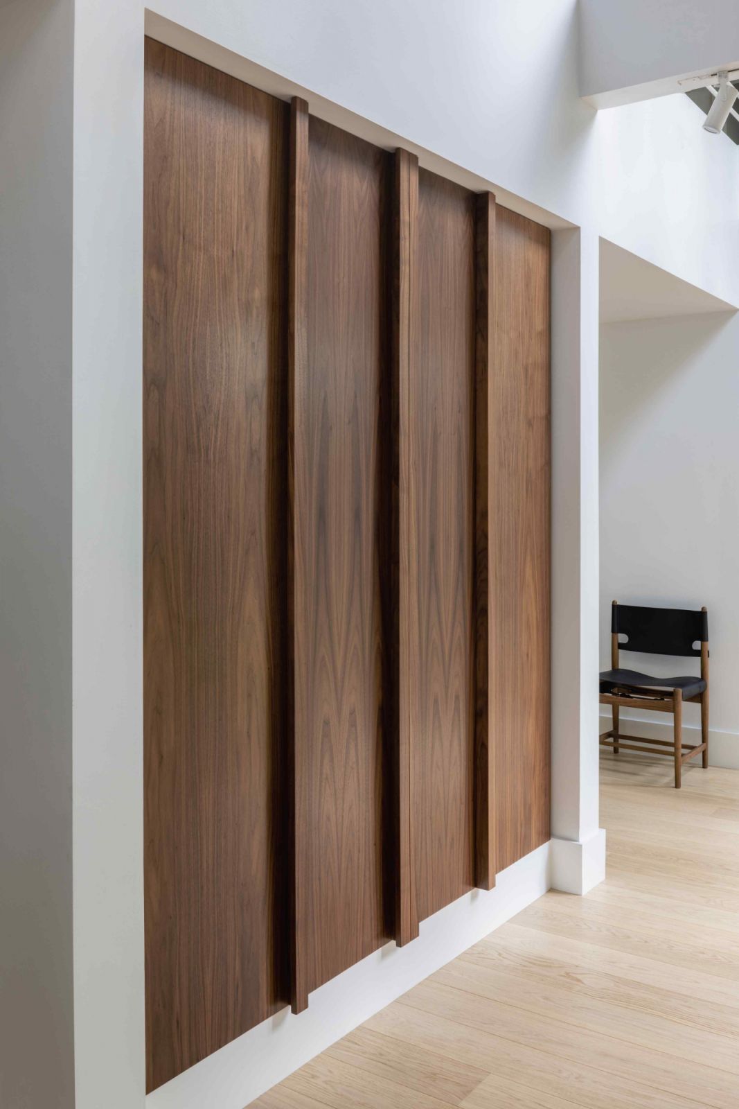 Walnut coat closet with integrated bevel pulls provided ample storage space