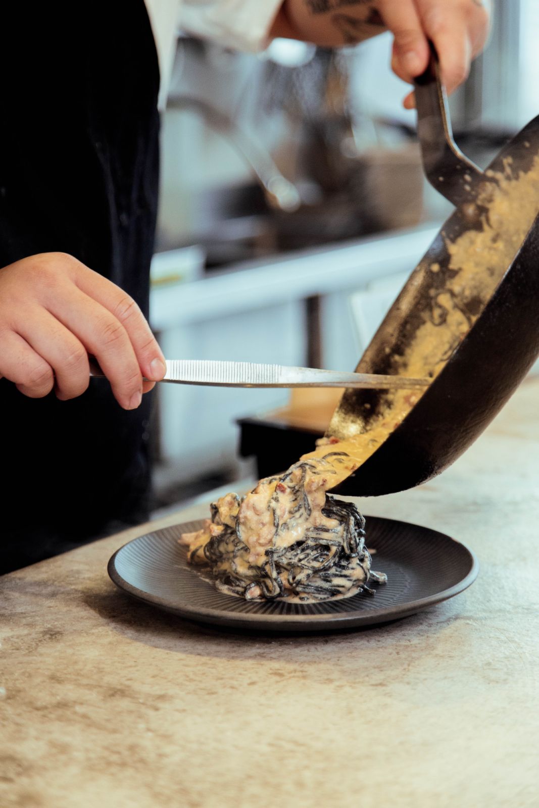 Plating up the famed smoked bacon carbonara using squid ink linguine