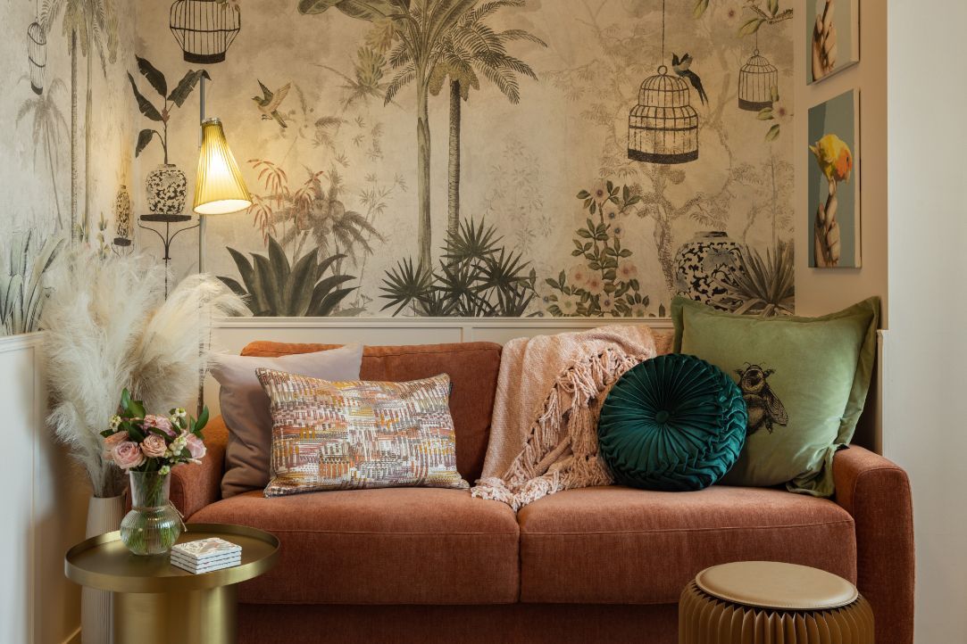 The botanical wallpaper enlivens the wife’s room, which is furnished with a dark-orange sofa and a brass side table