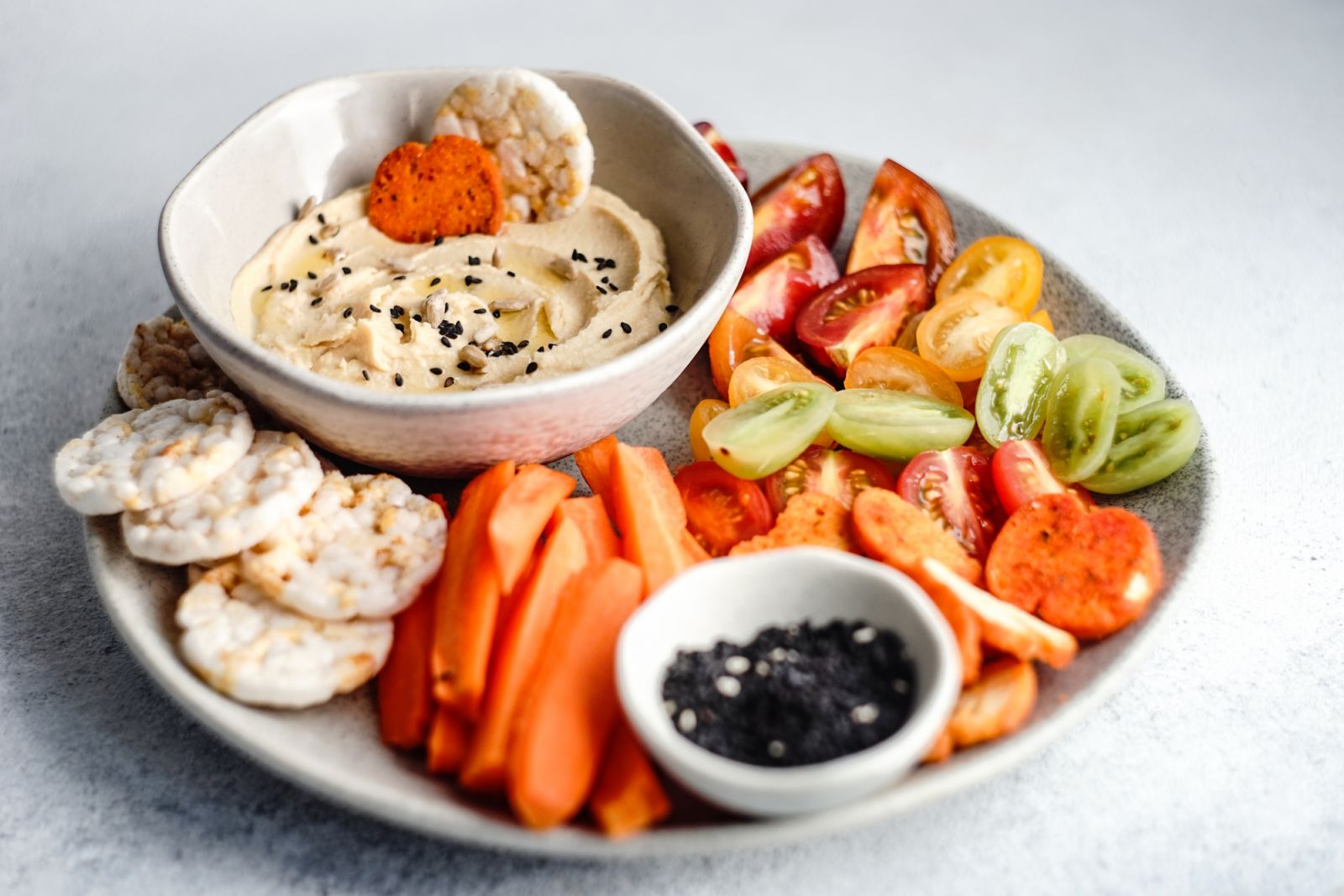 Hummus topped with sesame seeds accompanied by rice crackers and vegetable crudites
