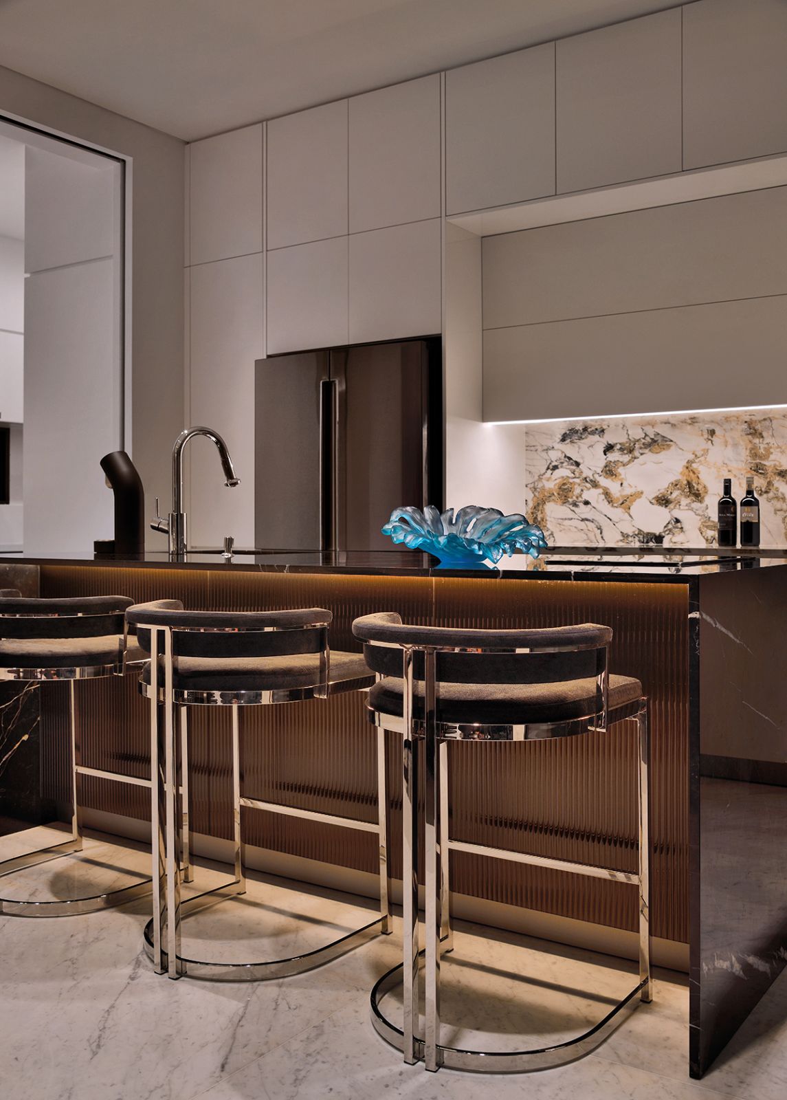 The gourmet kitchen features bronze fluted panels and the Étoile de Rex surface from Florim, matched with bar stools from Eichholtz