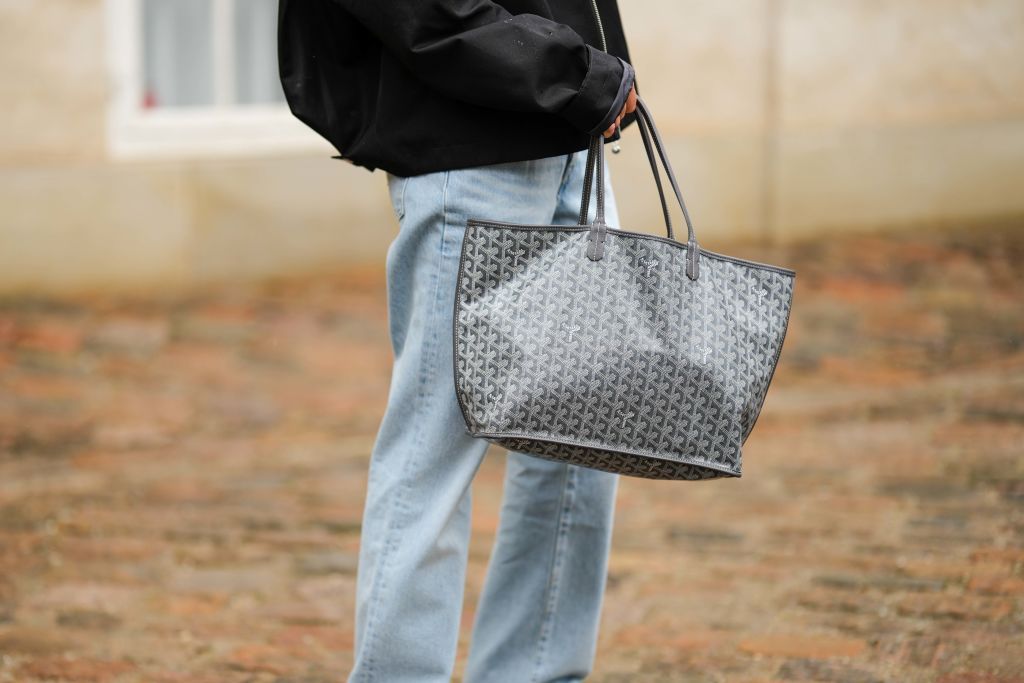 COPENHAGEN, DENMARK - AUGUST 09: A guest wears a black oversized bomber coat, a black and gray print pattern in coated canvas handbag from Goyard, blue faded denim large pants, outside Marimekko, during the Copenhagen Fashion Week Spring/Summer 2024 on August 09, 2023 in Copenhagen, Denmark. (Photo by Edward Berthelot/Getty Images)