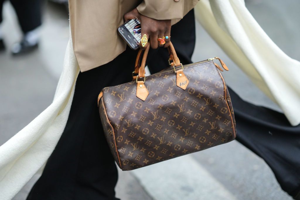 PARIS, FRANCE - JANUARY 23: A guest wears a beige blazer jacket, black flared pants, a white long scarf, a brown LV monogram print pattern Speedy handbag from Louis Vuitton, ring, outside Wooyoungmi, during Paris Fashion Week - Menswear F/W 2022-2023, on January 23, 2022 in Paris, France. (Photo by Edward Berthelot/Getty Images)