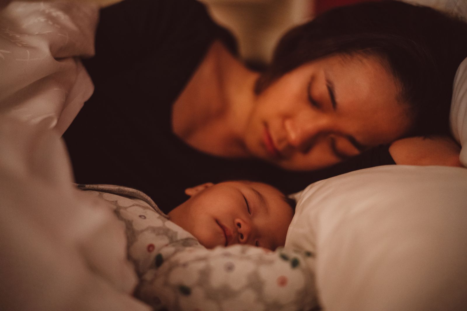 Pretty young mom sleeping soundly with her baby on the bed at night