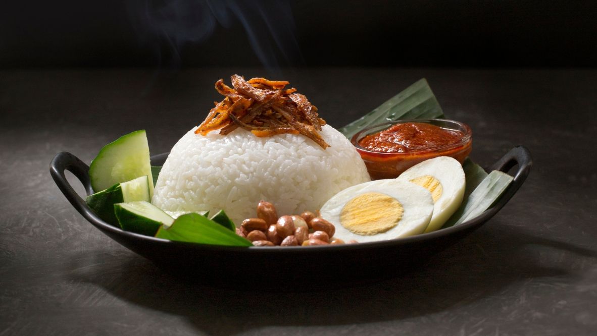 Steamy Malaysia traditional food "Nasi lemak" a on rustic black moody table top. Shallow depth of field image. "Nasi lemak" is a Malay fragrant rice dish cooked in coconut milk and pandan leaf. It is commonly found in Malaysia.