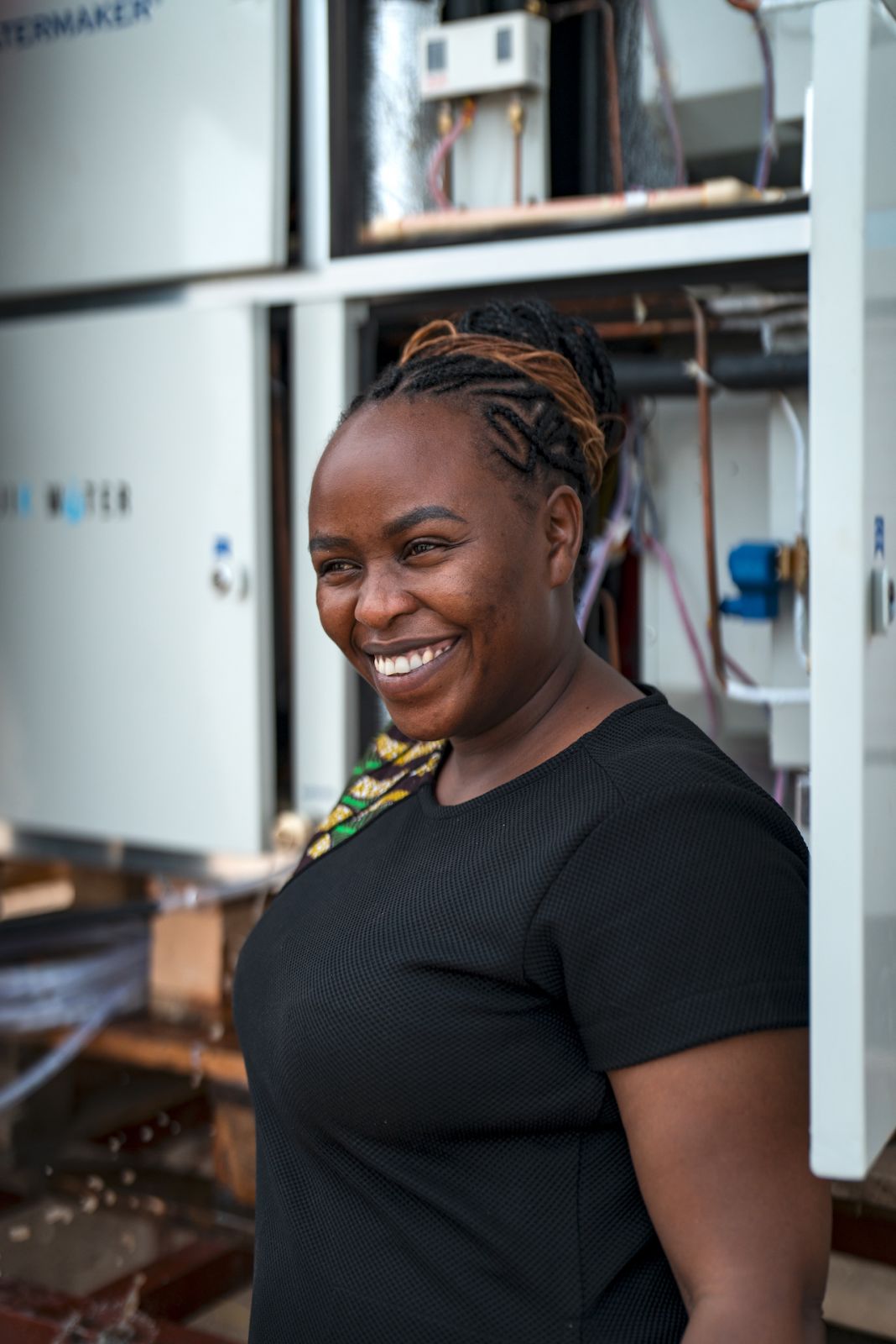 2023 Rolex Awards for Enterprise Laureate Beth Koigiin front of Majik Waterâs Atmospheric Water Generatorduring the installation process in Kakuma refugee camp.