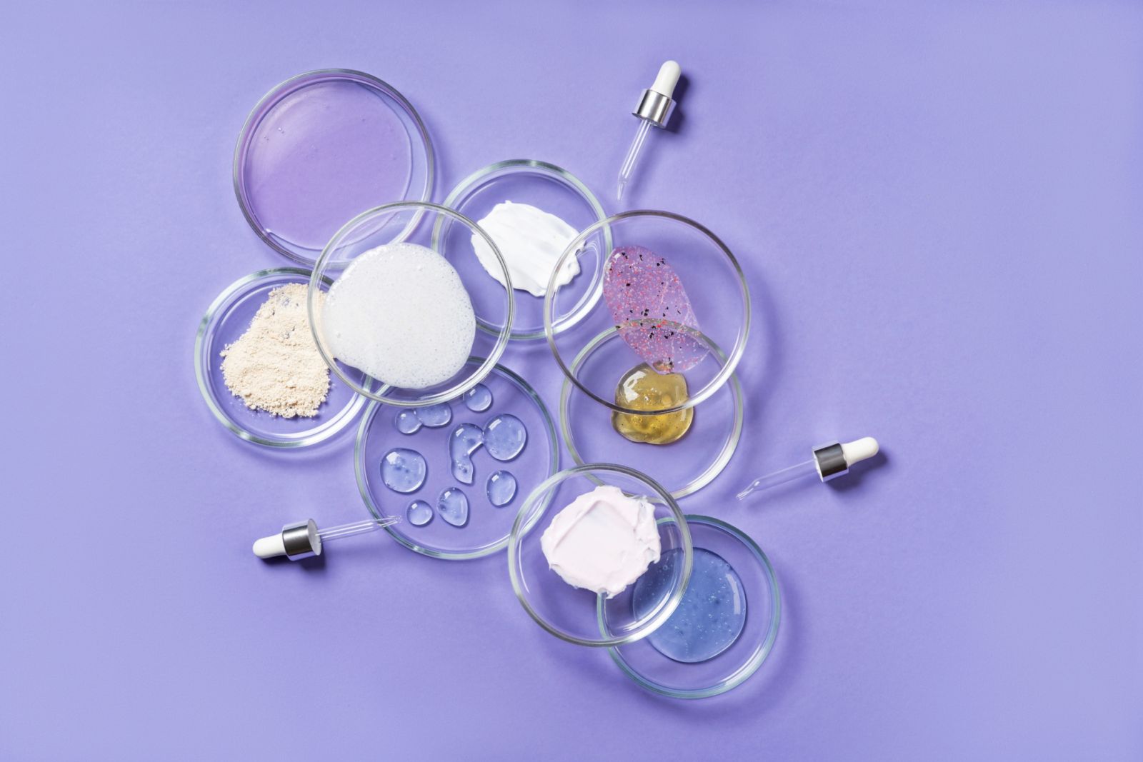 Cosmetic products, scrub, face serum and gel in many petri dishes on a pink background. Cosmetics laboratory research concept