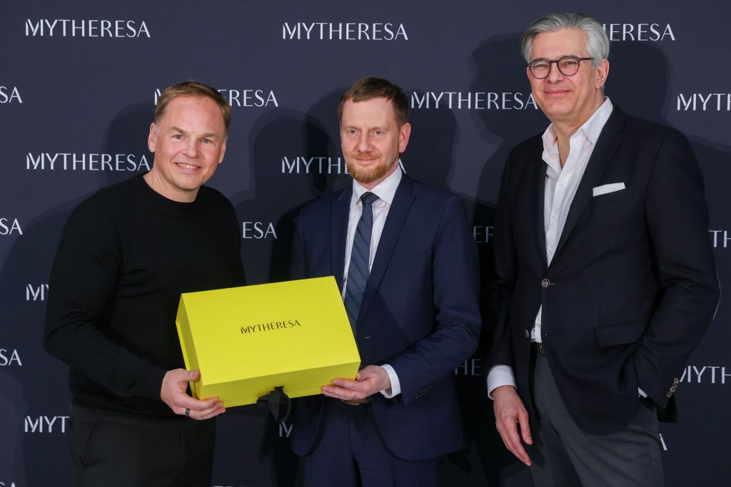 11 January 2024, Saxony, Schkeuditz: Sebastian Dietzmann (l-r), Head of Operations at Mytheresa, Michael Kretschmer (CDU), Minister President of Saxony, and Michael Kliger, CEO of Mytheresa, stand in front of a photo wall at the opening of the company's new logistics center, an online platform for luxury fashion. Covering an area of around 55,000 square meters, the center offers space for up to five million luxury items from the women's fashion and real jewelry categories. Thanks to its close proximity to t