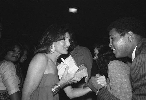 World Heavyweight Boxing Champ Muhammad Ali shakes hands with Jacqueline Onassis as they meet at pre-game bash, here 8/26, of the annual Robert F. Kennedy Pro-Celebrity Tennis Tournament to be held at Forest Hills 8/27. The tournament is a charity affair which supports many social and educational programs for underprivileged children and is the main fund-raiser for the RFK memorial.