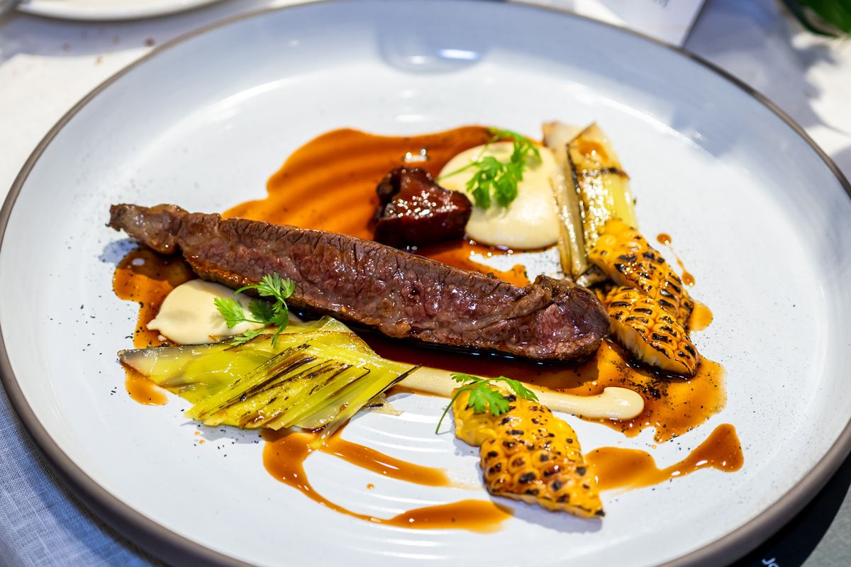 The wagyu beef steak, comprising wagyu beef flank steak, braised beef cheek Japanese corn, corn crème, roast baby leek and leek ash