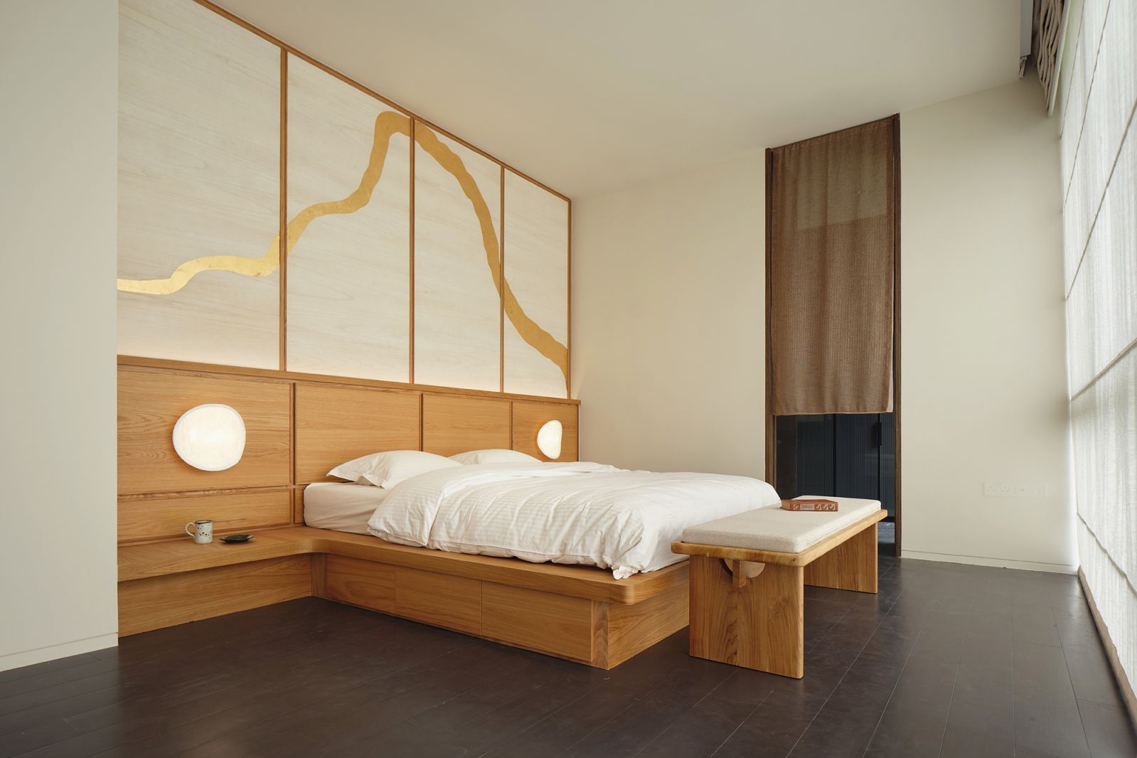 The bedroom features a platform bed with storage, a bench with traditional Chinese joinery details, handmade gold foil wallpaper and a pair of New Works Tense wall lamps from Made & Make