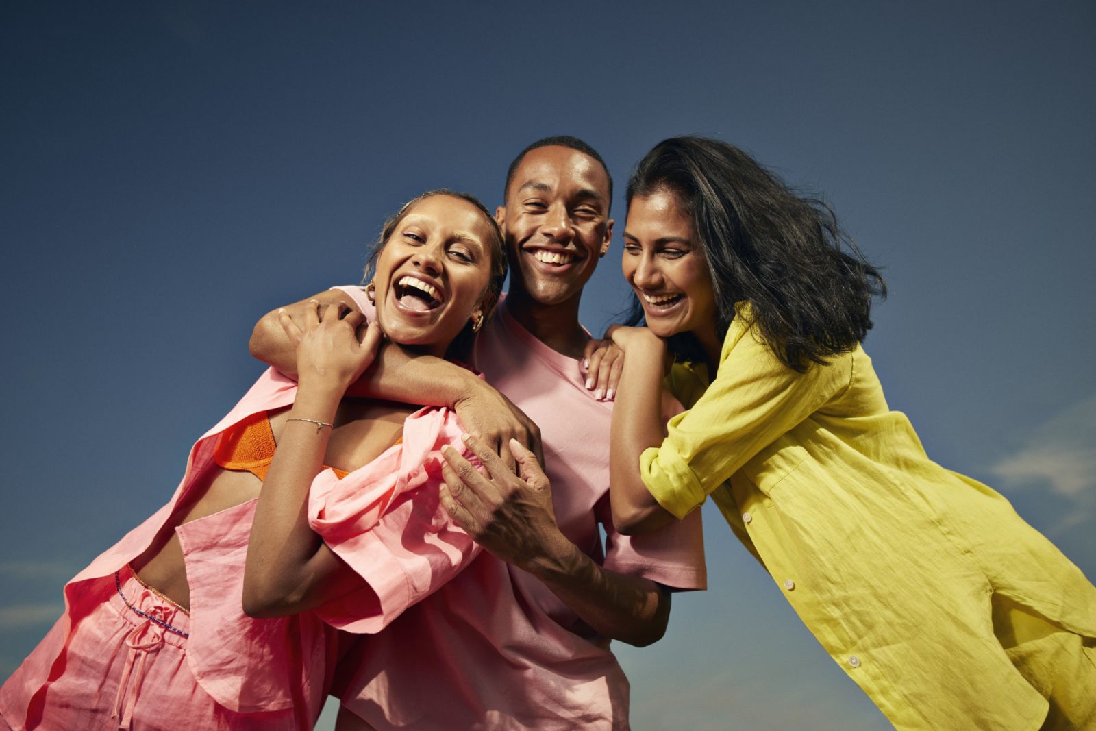 Low angle portrait of cheerful friends laughing while standing against sky