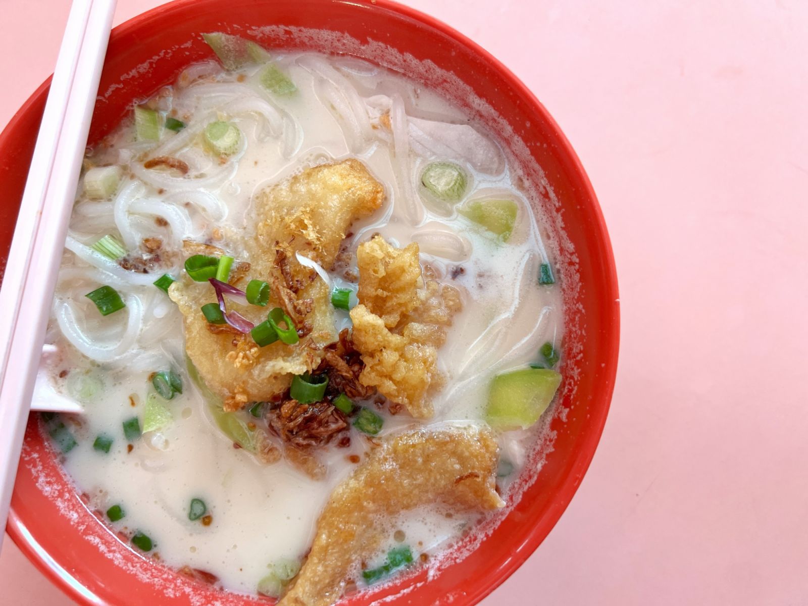 Overhead view of a bowl of Chinese fried fish soup with sliced cucumber and rice noodle from Singapore local food center