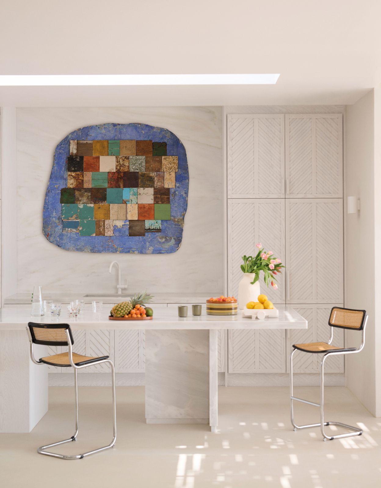 An artwork by Greek artist Rena Papaspyrou serves as a lively focal point in the neutral-hued kitchen