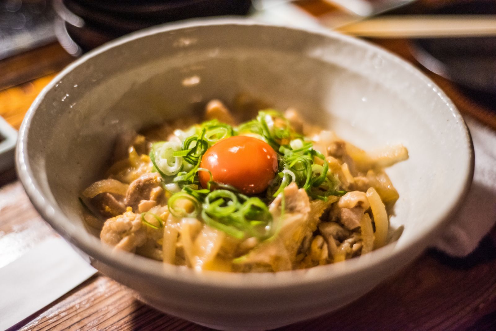 Close up of a bowl of Kamatama udon topped with raw egg and chives at a Yakiniku restaurant in Kyoto, Japan.
