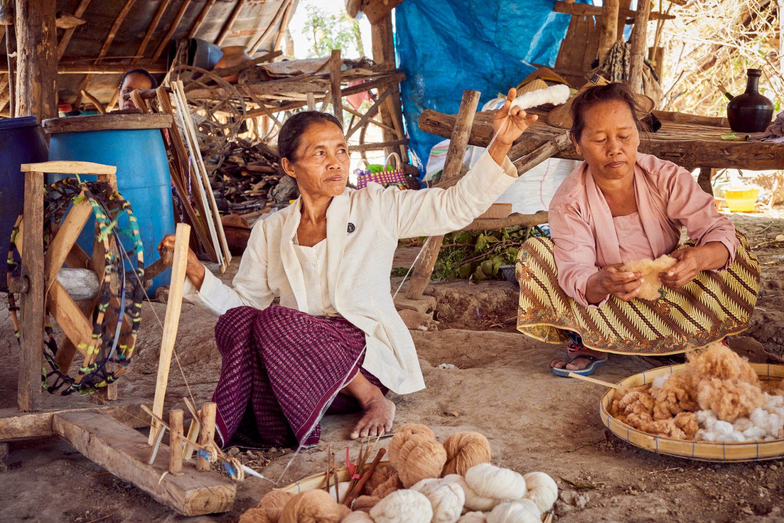 SukkhaCittaâs Ibu Kasmini, an Indonesian farmer who has inherited her farming practices from her grandmother, using a spinning wheel to turn cotton into threads while Ibu Karmini prepares the cotton behind her.