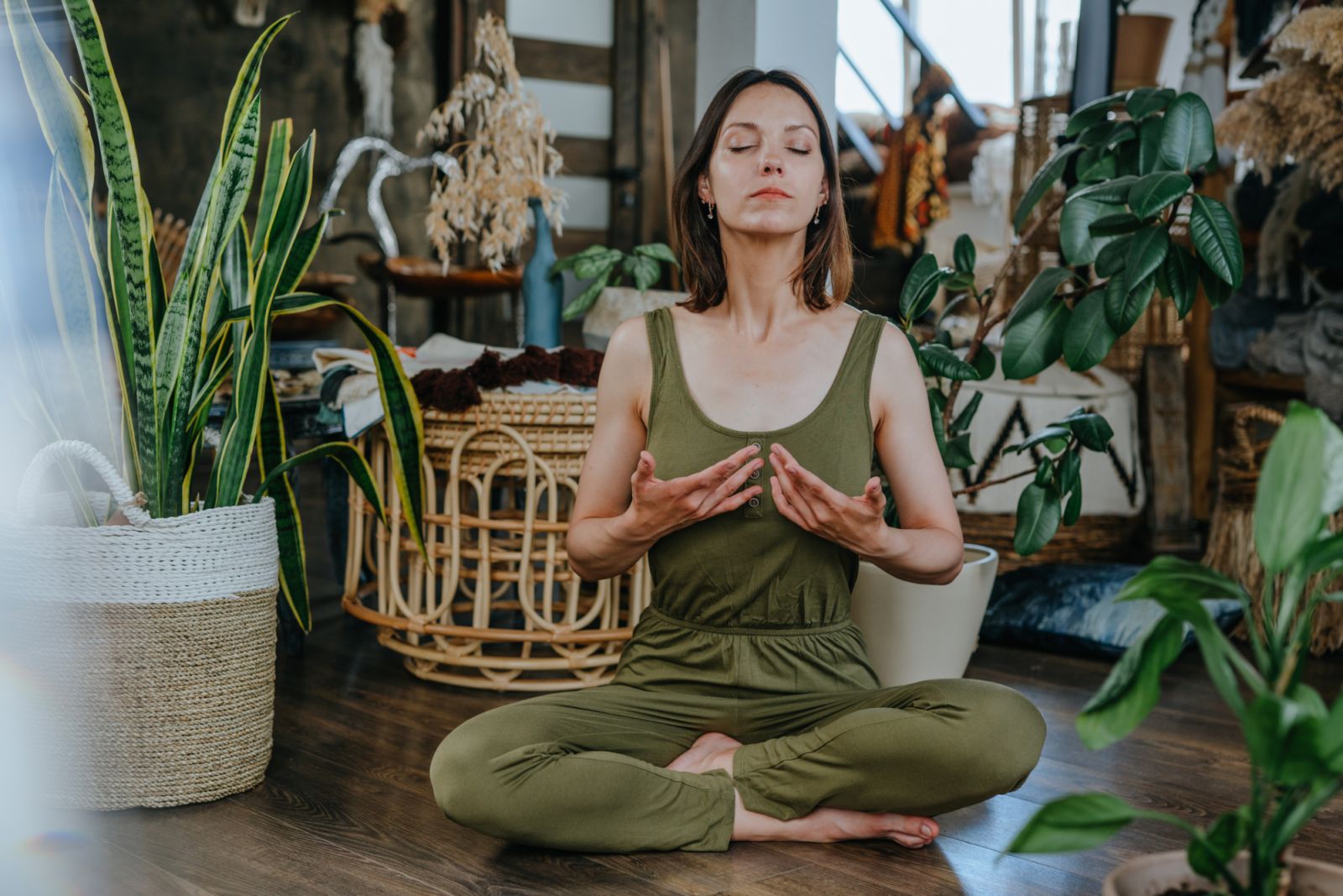 Young woman with closed eyes practising yoga breathing exercises sitting Lotus pose at home. Selfcare and wellness concept. Selective focus.