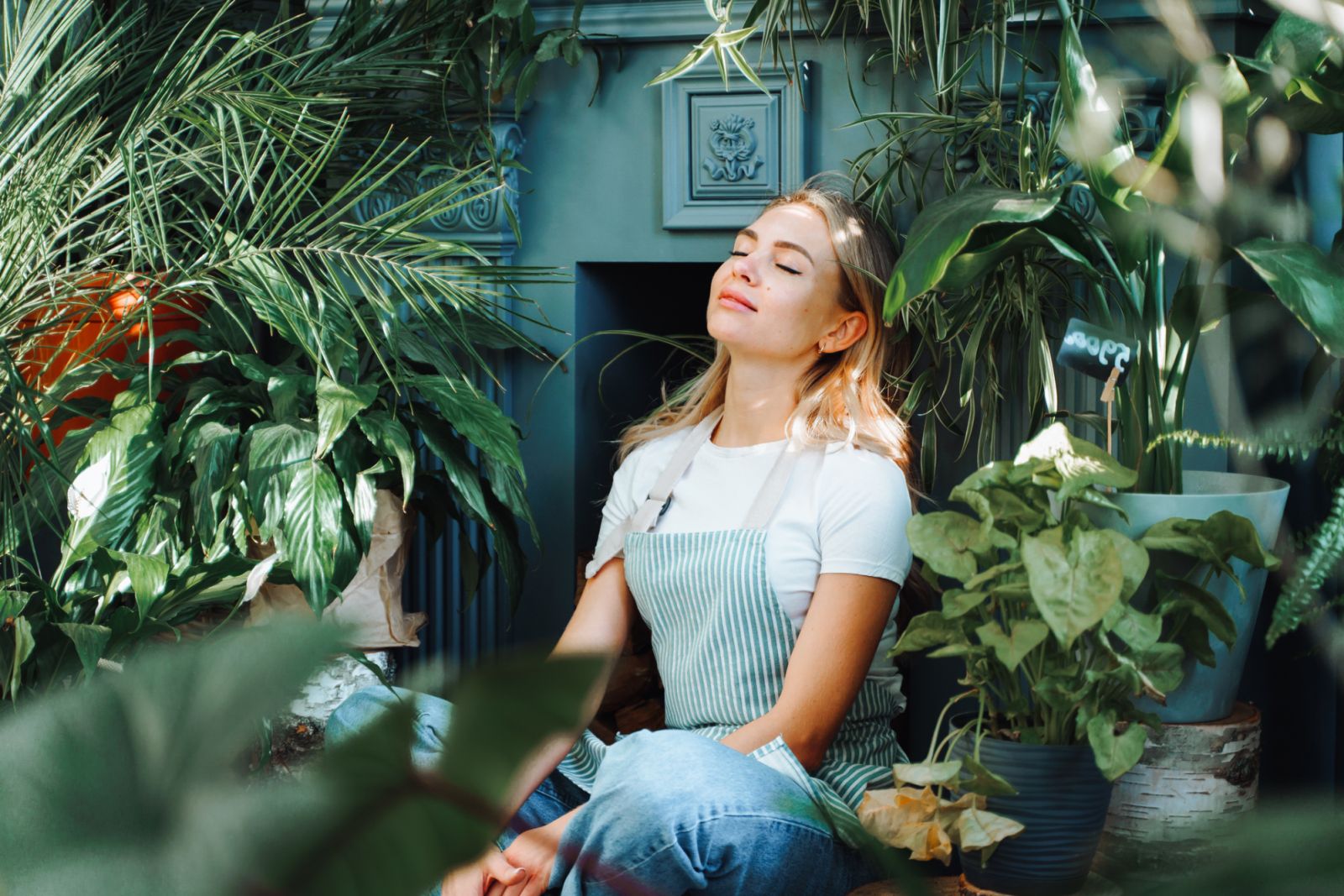 Relaxing and meditating smiling female near green plants and flowers, joying scent. Break and napping before new customers