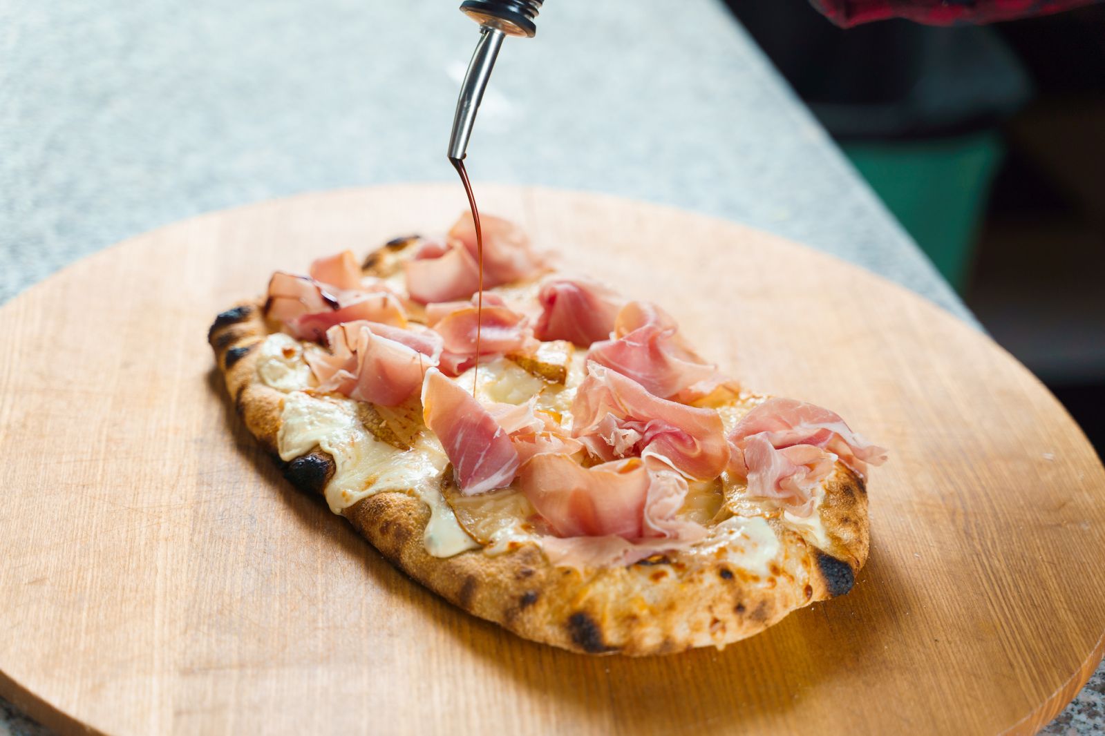 Chef cooking pinsa romana with pear, cheese, prosciutto in delivery box. Scrocchiarella gourmet italian cuisine Holding traditional dish. Food delivery from pizzeria.