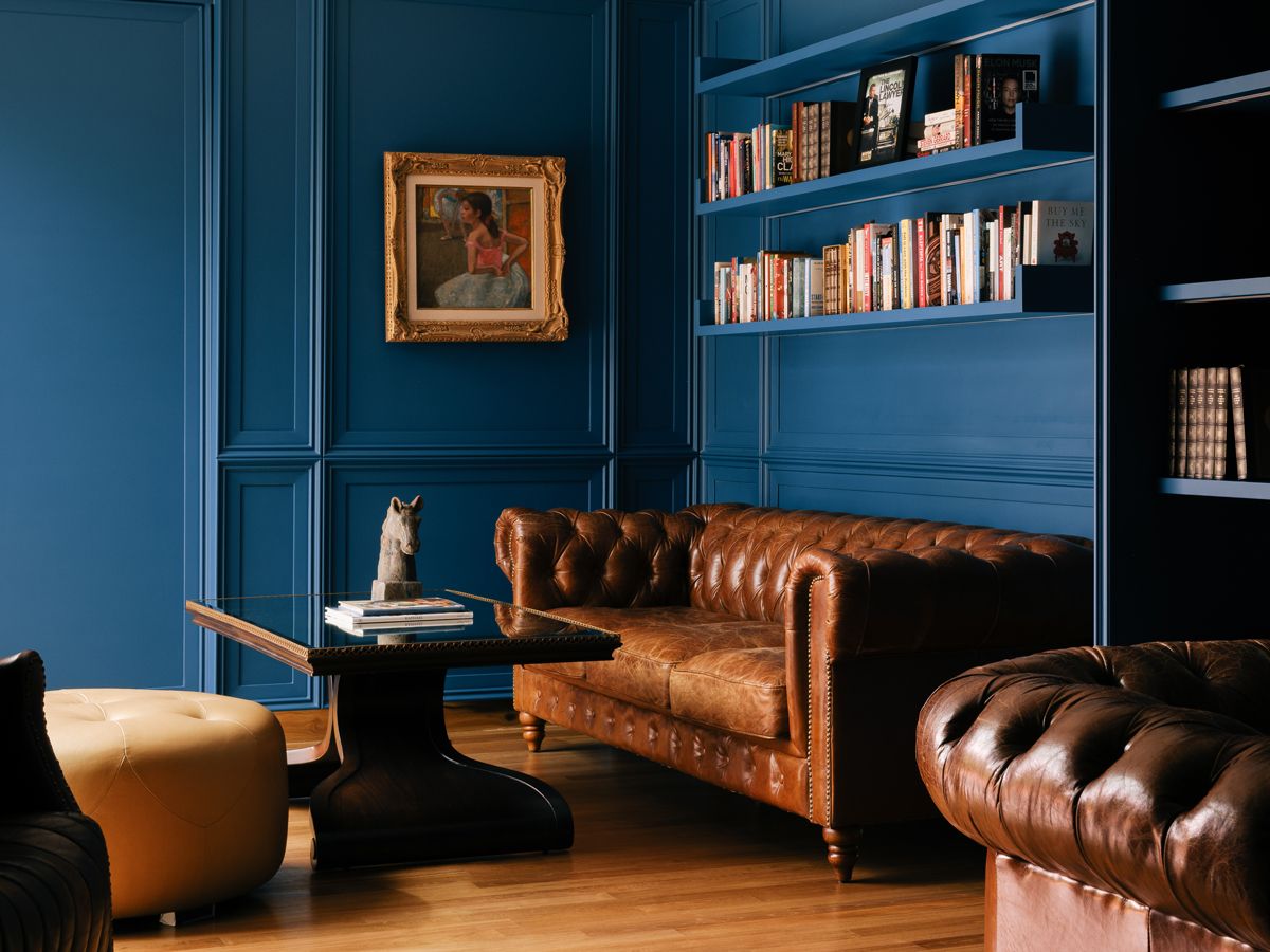 Panelled walls in blue make the gilded painting and classic Chesterfield sofa pop