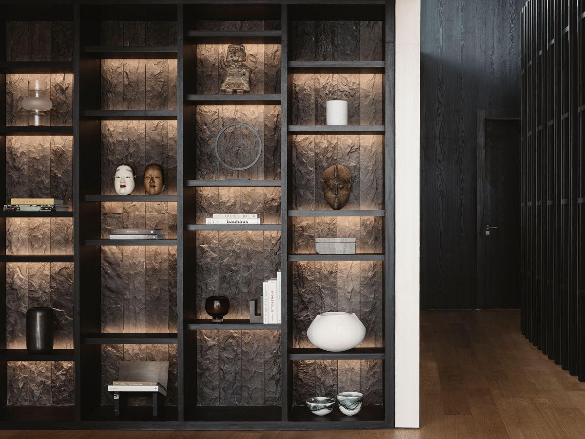 A dark feature wall clad in a combination of timber veneer, granite and stainless steel, along with backlit shelves housing a mix of books and exotic curios, lend a hint of intrigue to the home (Photo: Studio Periphery)
