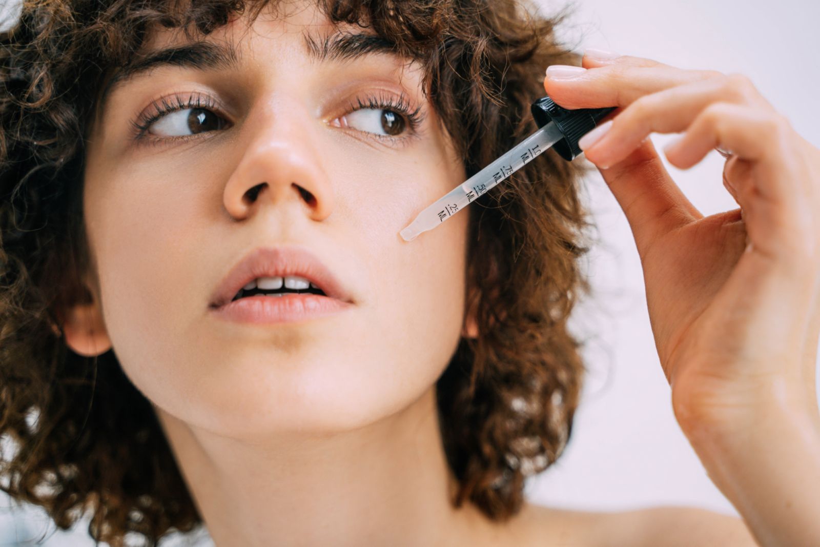 A beautiful young woman applies serum to her face with a pipette. Close-up portrait.