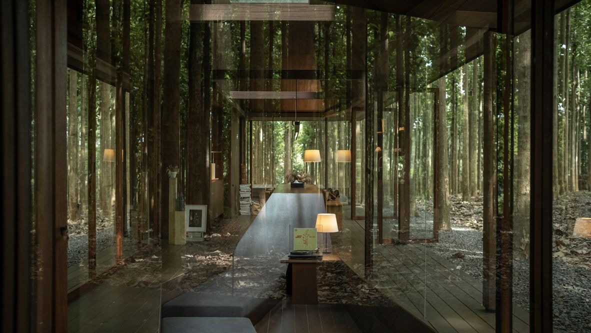The glass-encased sunken living room in the villa retreat features a sloping plane that is part of the adjoining dining zone’s elongated table