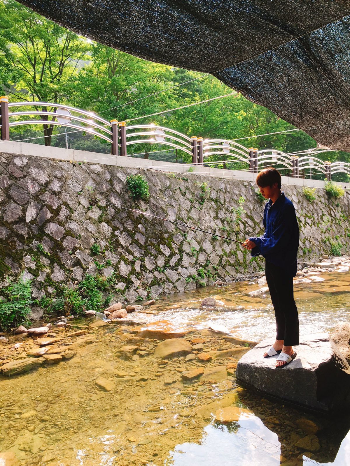 Jin fishing while wearing Givenchy slides (image courtesy of X / @bts_bighit)