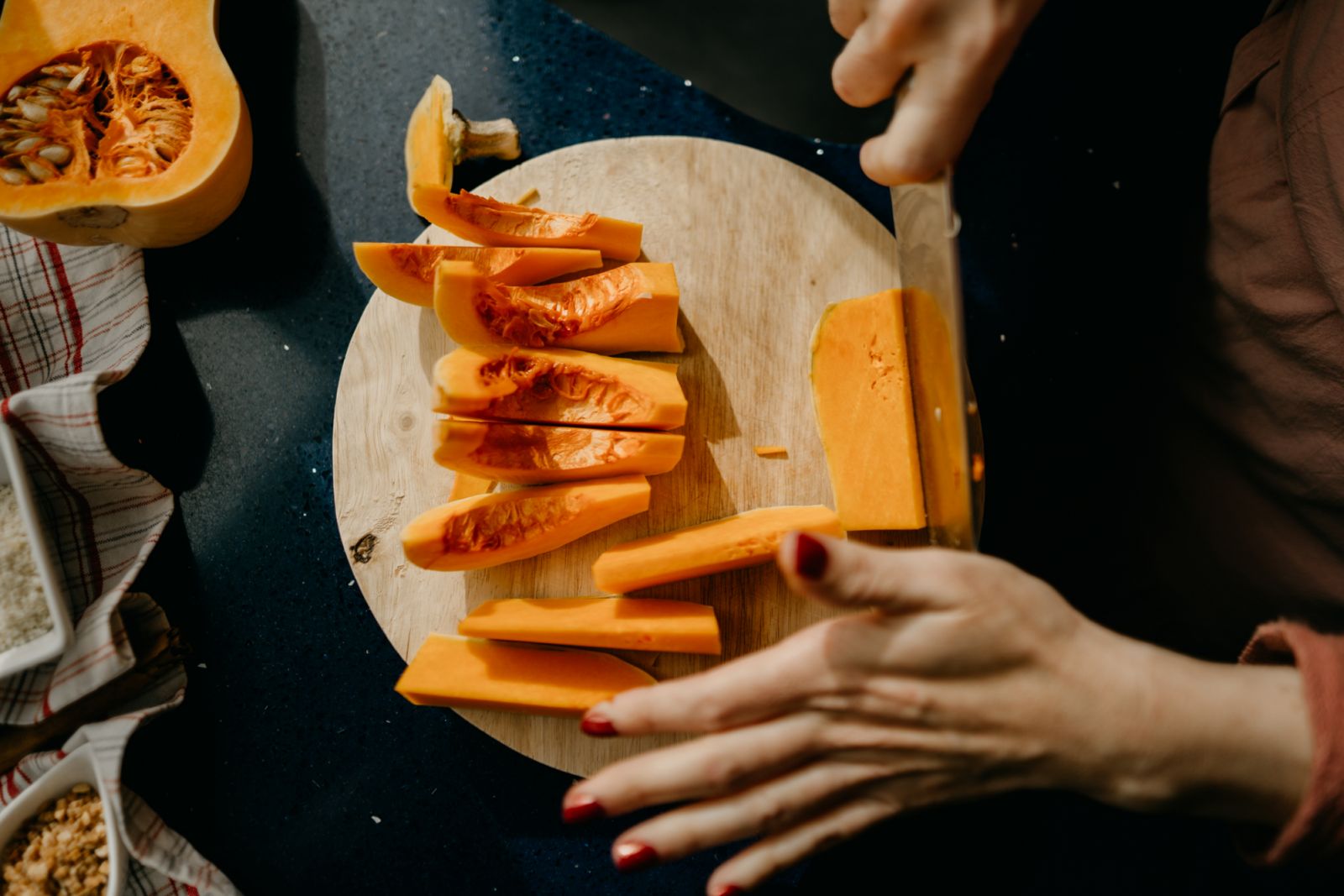 Caucasian woman slicing a Butternut Squash on a wooden cutting board. High view