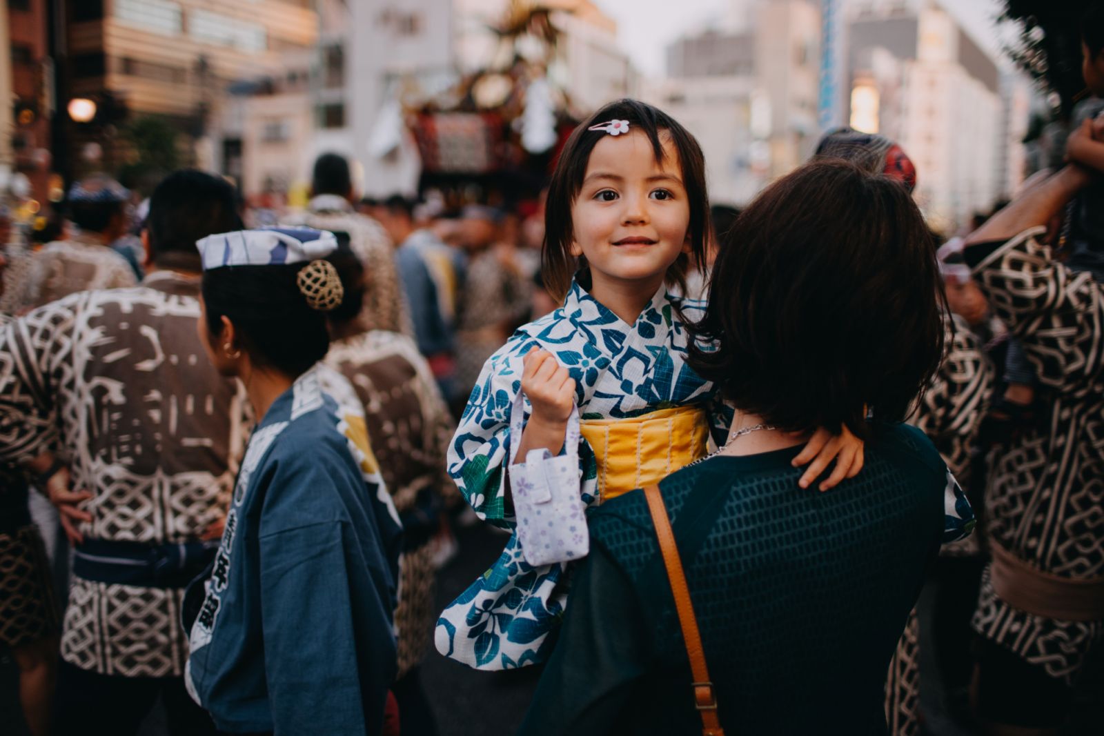 Adorable 3 year old girl in Yukata carried by mother at traditional Japanese festival