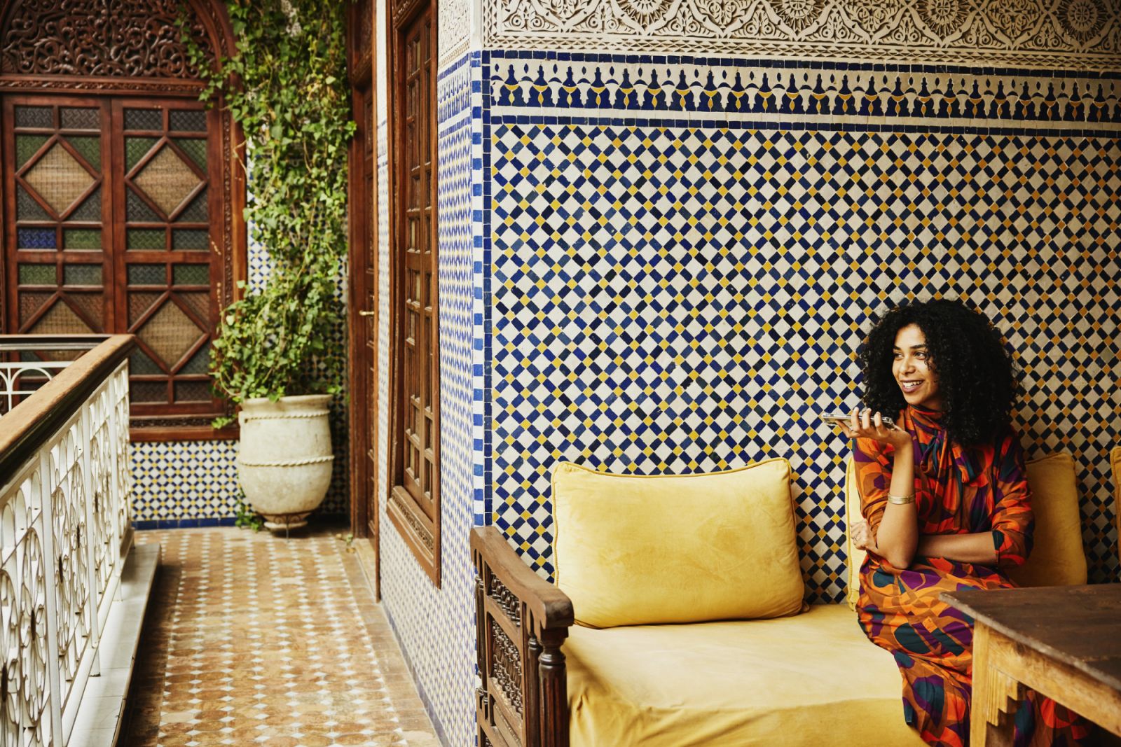 Wide shot of smiling woman relaxing in alcove of ornately decorated riad while on vacation in Marrakech
