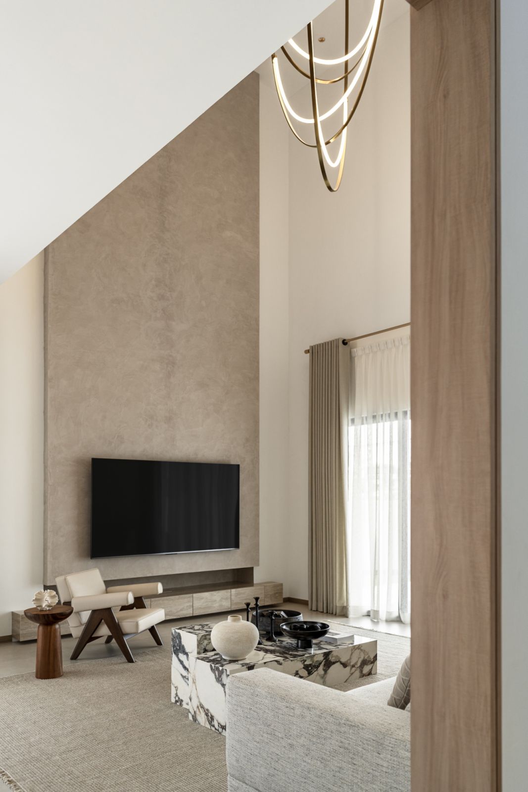 Double-height living room with sculptural light fixture, textured walls, and minimalist decor