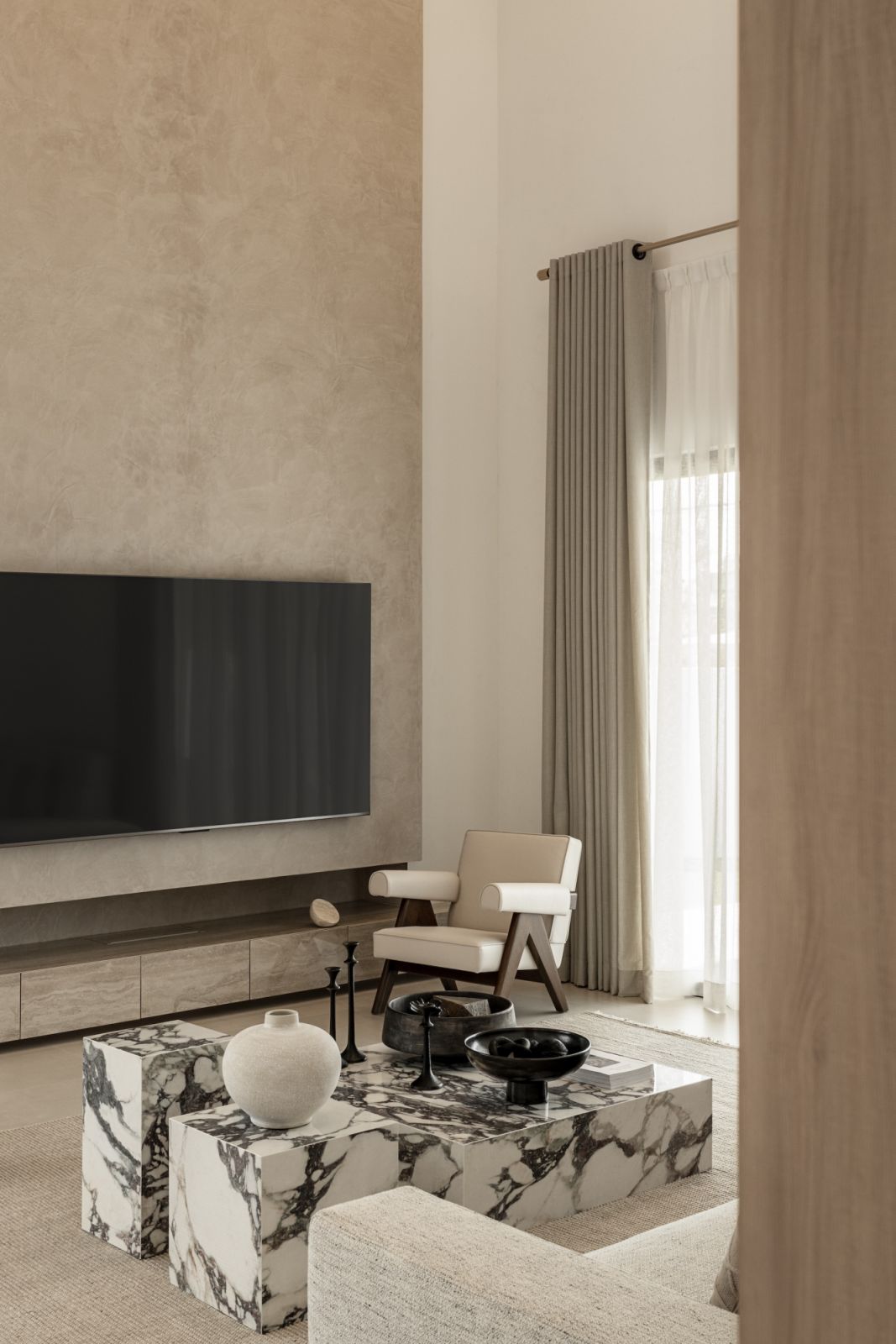 Contemporary living space featuring marble coffee tables, textured accent wall, and floor-to-ceiling curtains