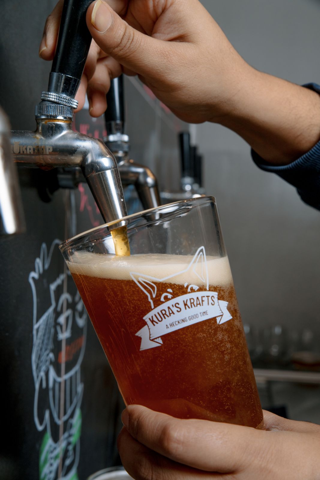 A craft beer being poured into a glass with an illustration of Kura