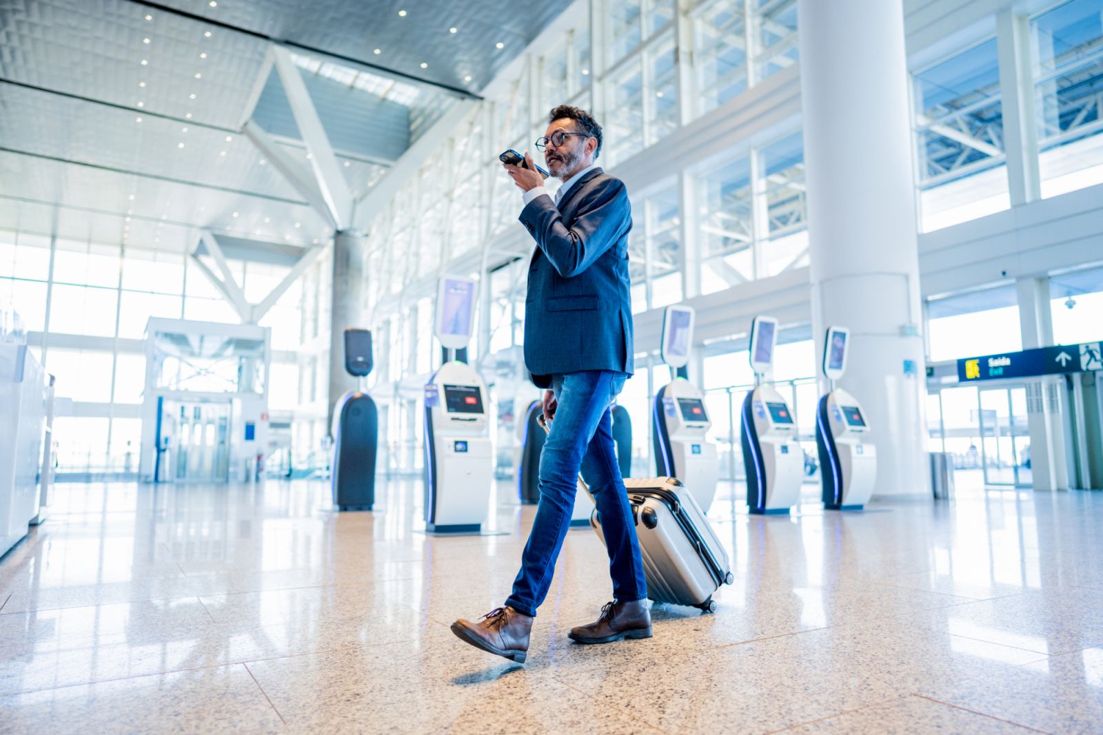 Businessman walking and sending audio message using mobile phone at the airport