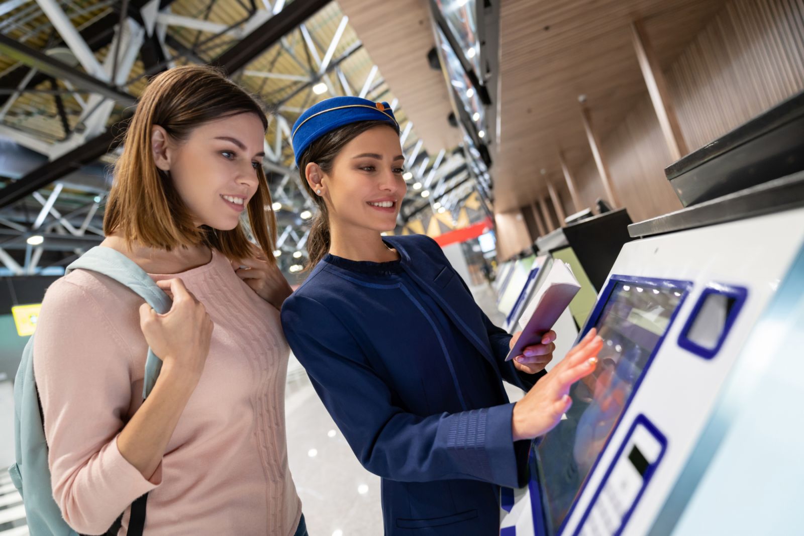 Woman helping a female traveler do the self check-in at the airport using a machine - travel concepts