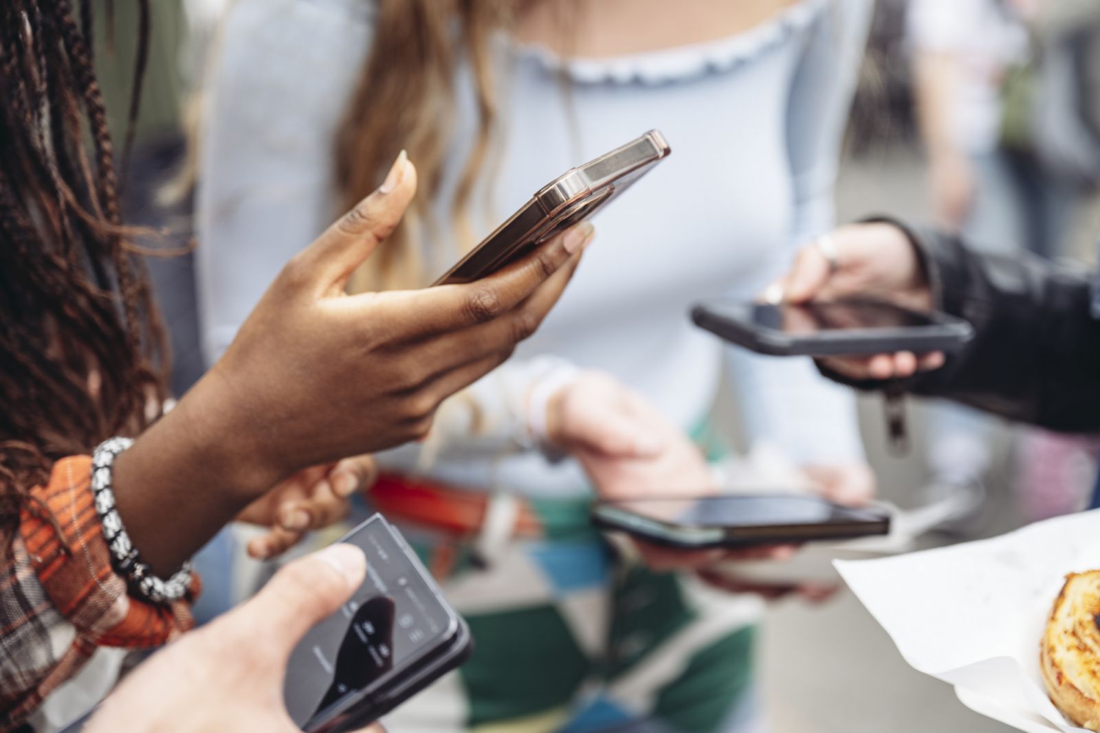 Focus on teenage Black woman standing with friends, all using their portable devices.