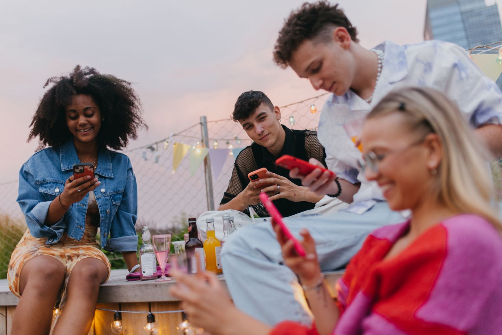 Generation z friends hanging out together outdoors in the city during summer break. Young stylish zoomers spending time online during party on rooftop terrace. Concept of power of friendship and social strength of gen Z.